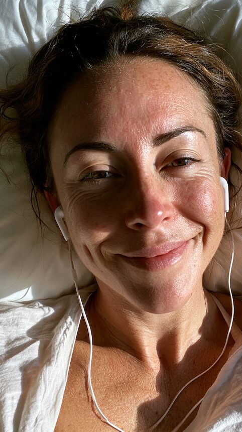 Relaxed smiling woman lying on a white pillow wearing earphones